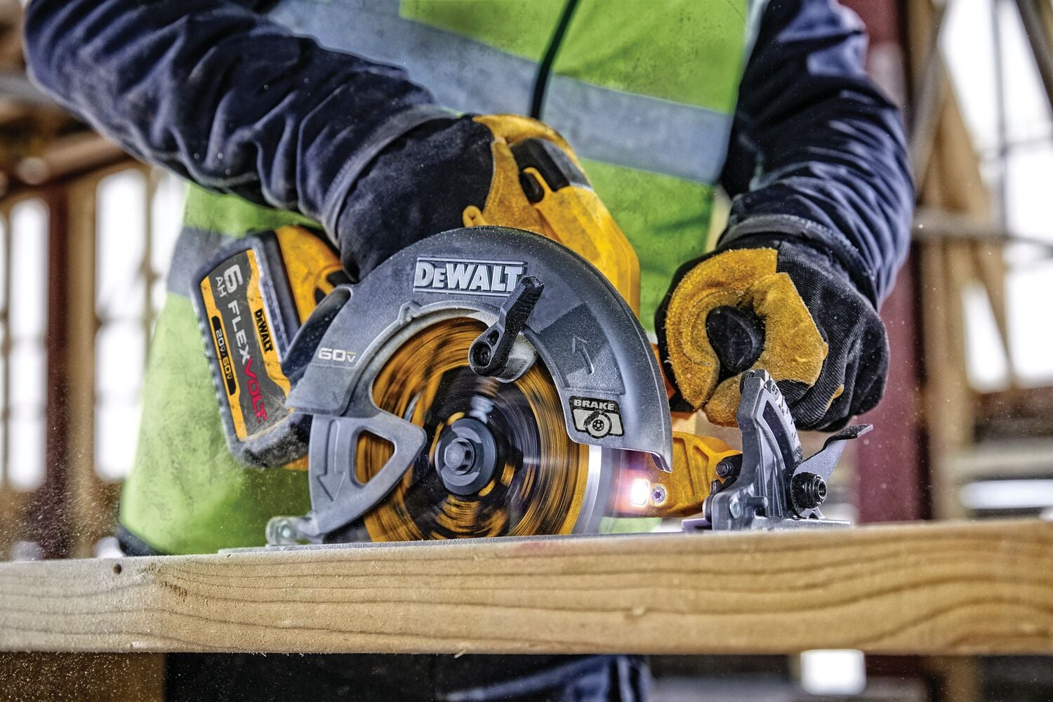 Primer plano de una persona usando una sierra circular DEWALT para cortar un trozo de madera. La persona lleva guantes de trabajo amarillos y un chaleco de seguridad brillante, con un sitio de construcción visible en el fondo.